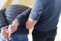 osoba zatrzymana z założonymi kajdankami na ręce trzymane z tyłu jest prowadzona przez policjanta