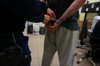 policjant zakłada kajdanki na ręce z tyłu zatrzymanemu