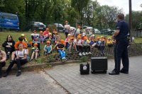 policjant prezentuje walizkę antynarkotykową, dzieci w plenerze siedzą i słuchają