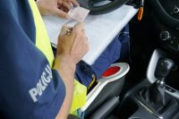 policjant trzyma prawo jazdy i wpisuje dane do notatnika