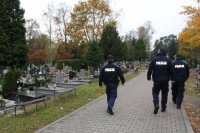 troje policjantów widocznych tyłem patroluje cmentarz