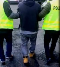 policjanci prowadzą zatrzymanego mężczyznę, który ma założone kajdanki na rękach i nogach