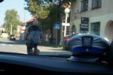 policyjna czapka, przed radiowozem jedzie mężczyzna na rowerze