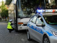 policjant sprawdza koła w autobusie- jest w pozycji siedzącej w tle, w pierwszym planie radiowóz policyjny