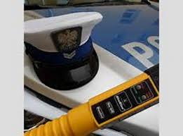 policyjna czapka z białą obwolutą, żółte urządzenie do badania trzeźwości leżą na masce policyjnego radiowozu