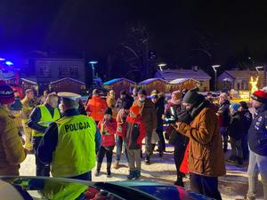 grafika-noc, śnieg, policjant wręcza odblaski, widoczne samochody na płycie rynku