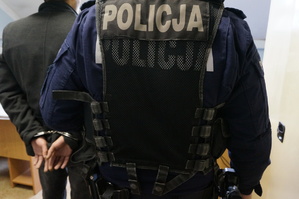zdjęcie-policjant prowadzi osobę z kajdankami na rękach z tyłu